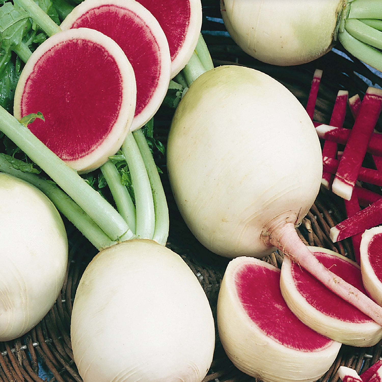 A collection of watermelon radishes with a green stem, white skin, and bright red flesh, some whole and some cut to show the interior.