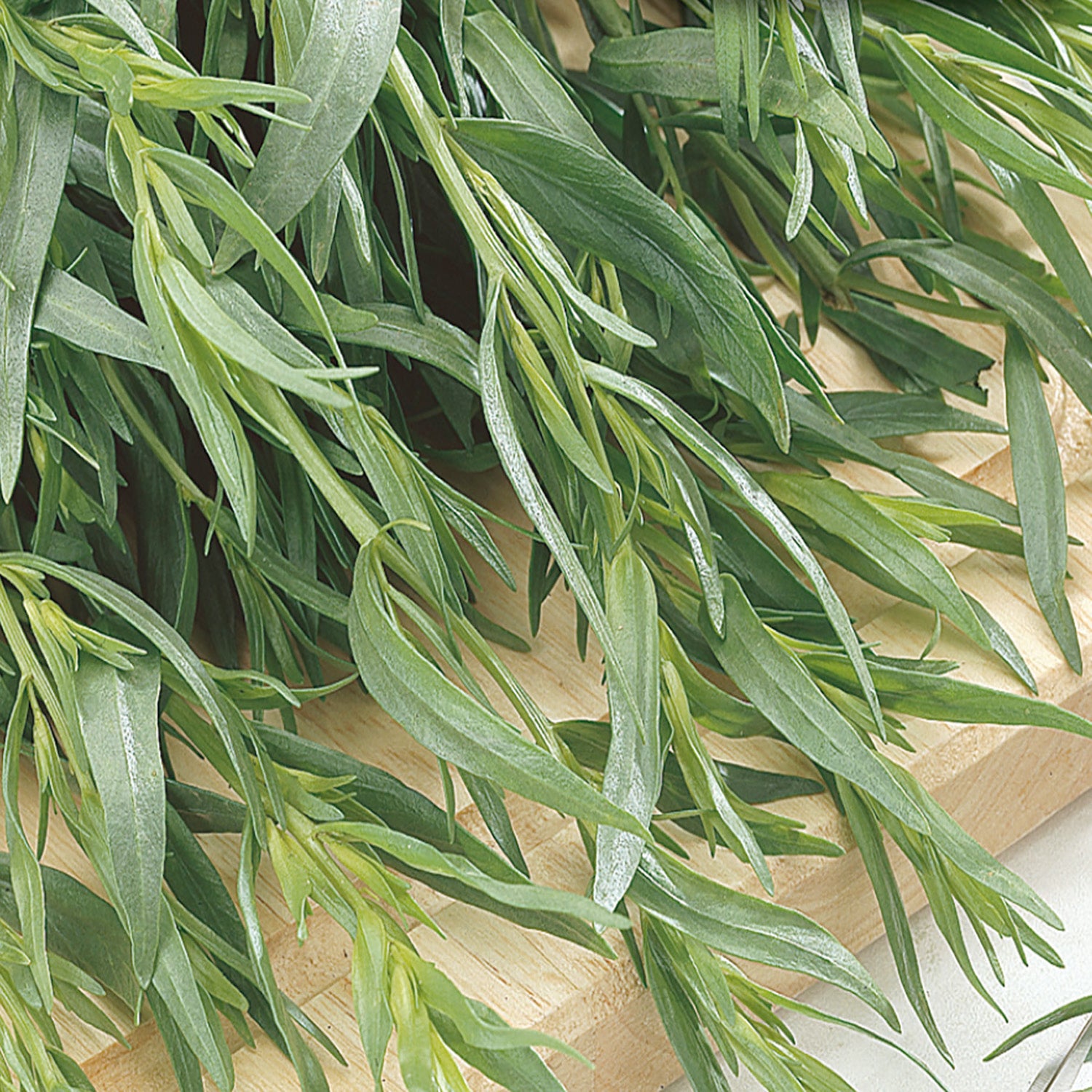 A close-up of fresh green Russian Tarragon leaves on a wooden surface.