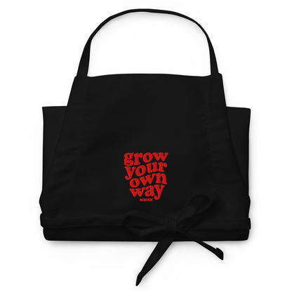 Black apron with red text 'grow your own way' on a white background