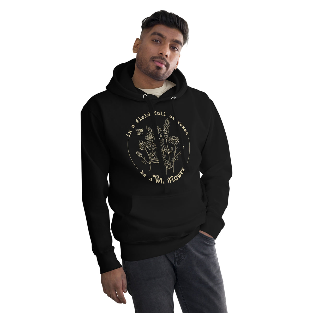 A man wearing a black pullover hoodie with a gold graphic print on the chest that reads 'In a field full of flowers be a wildflower with a floral illustration, set against a plain white background.