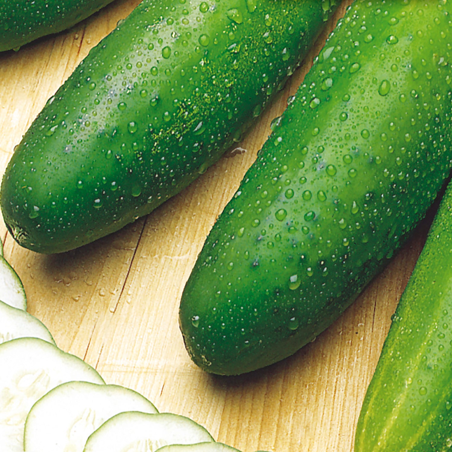 Fresh green cucumbers with water droplets on them, placed on a wooden surface.
